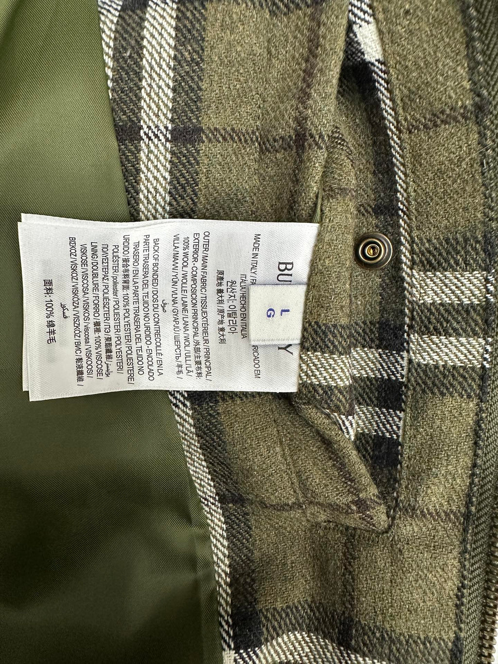 Olive green plaid jacket care label on inner seam near metal button