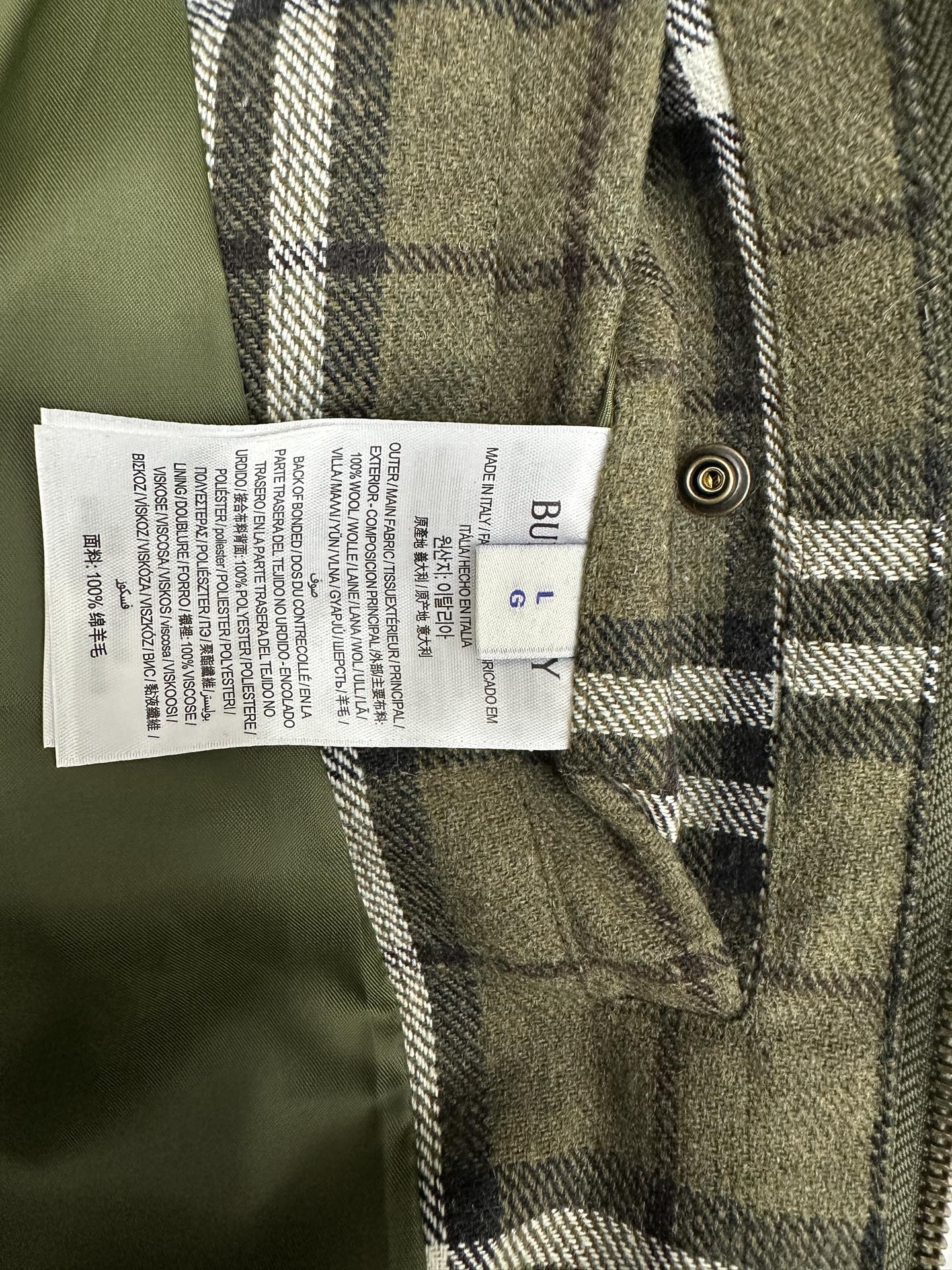 Olive green plaid jacket care label on inner seam near metal button