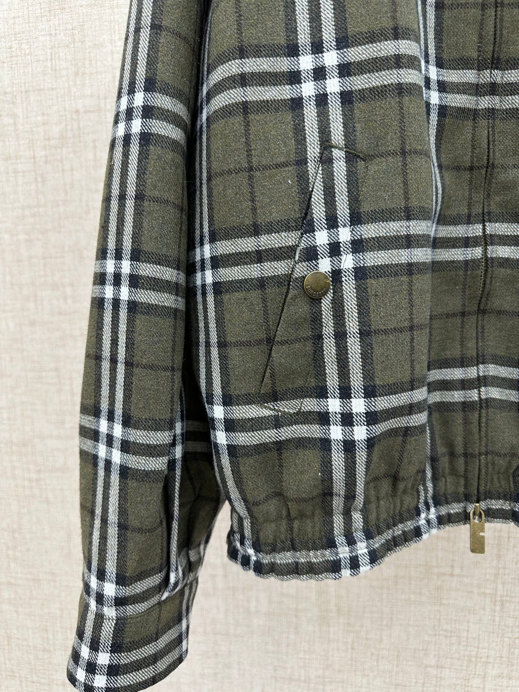Olive green and black plaid jacket sleeve with cuff and stitched front pocket detail