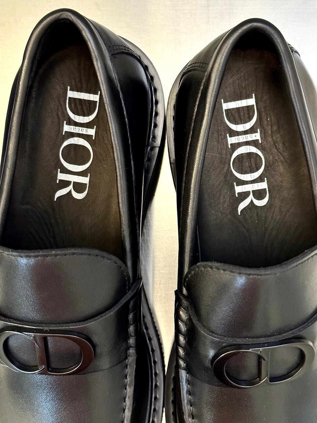 Close-up of dark leather Dior loafers showing printed DIOR branding and D buckle