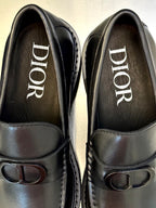 Close-up of dark leather Dior loafers showing printed DIOR branding and D buckle