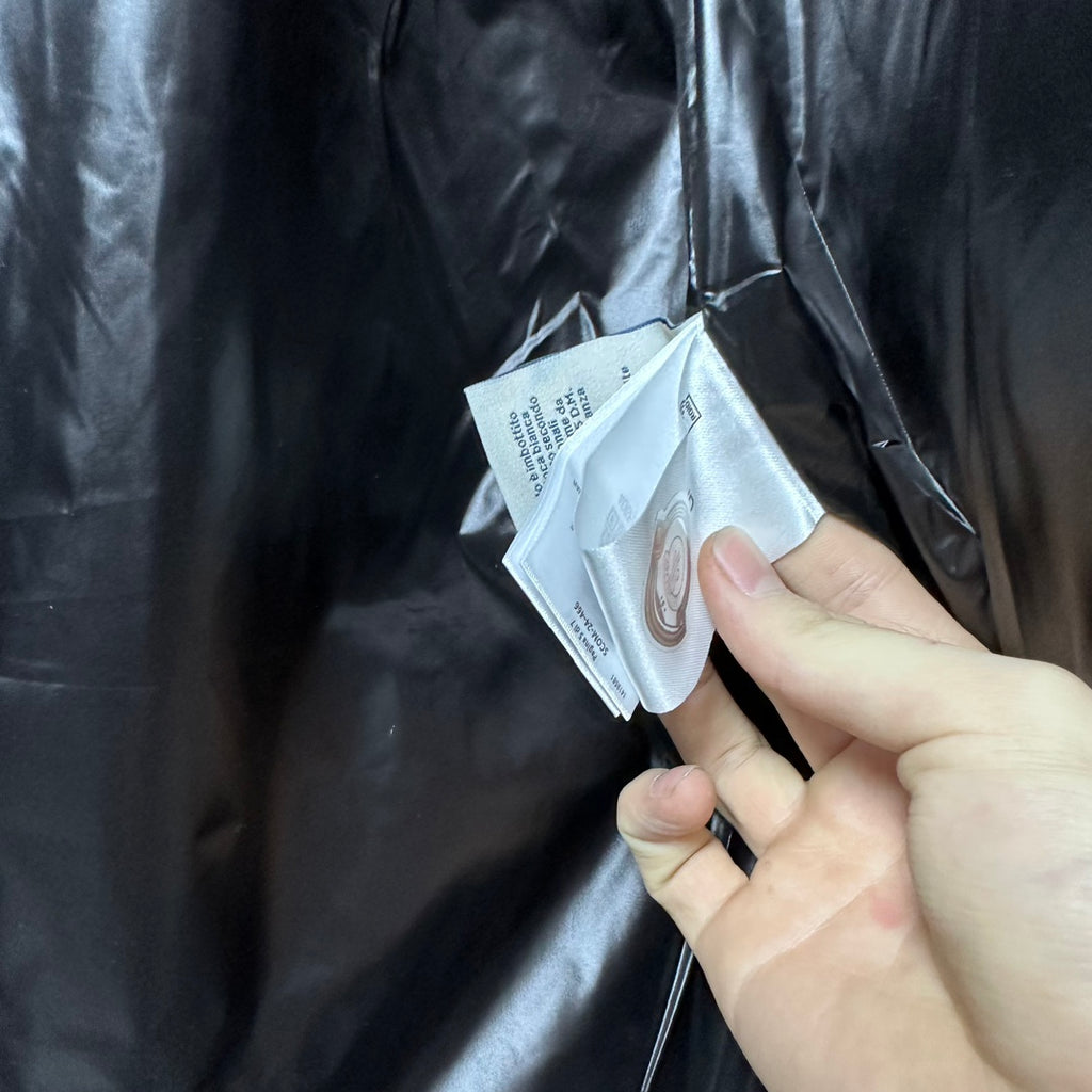 Moncler puffer jacket fabric close-up with white care tag and hand holding the tag