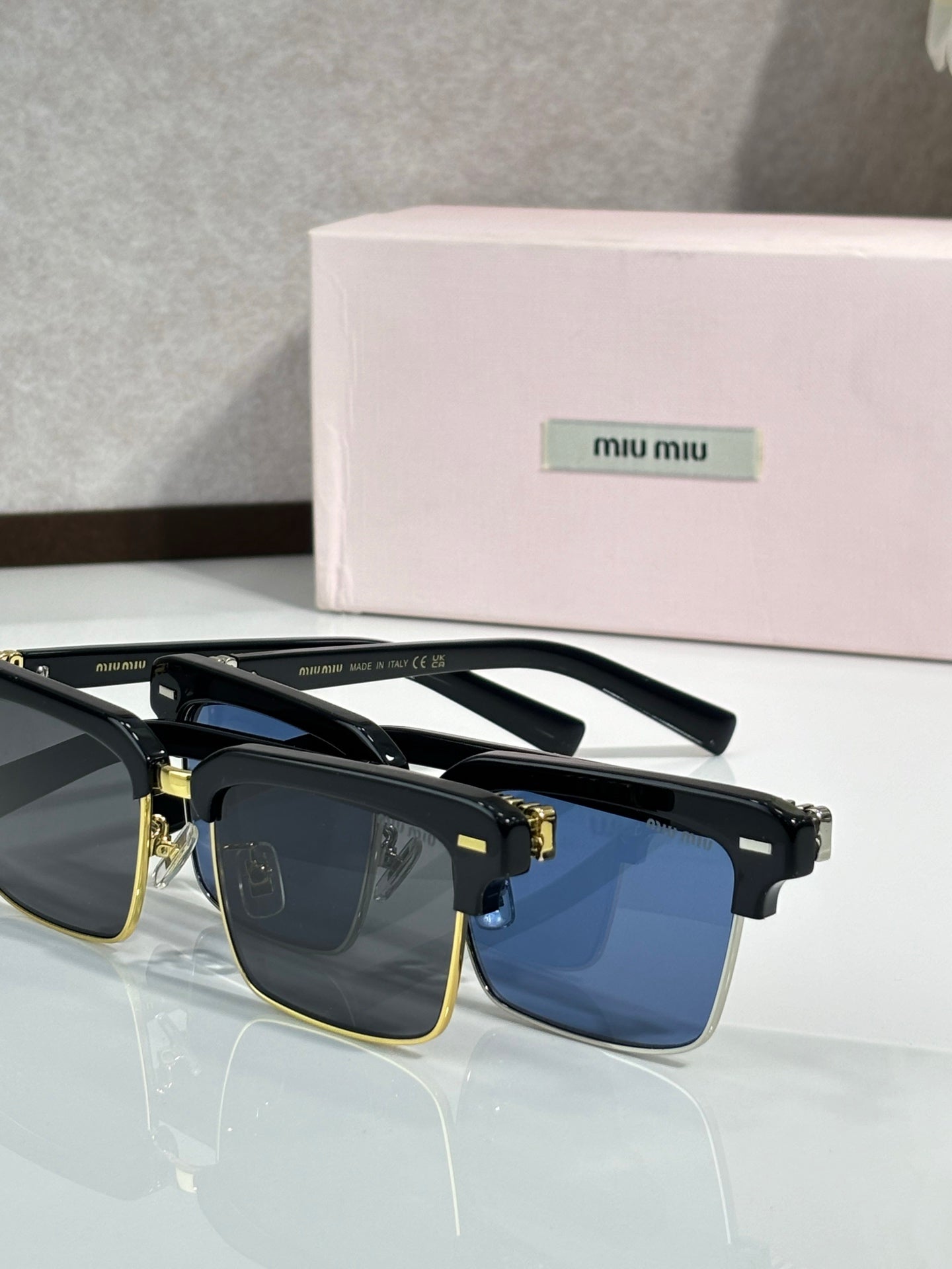 Square sunglasses with black frame, gold accents, blue tinted lenses, visible temple details
