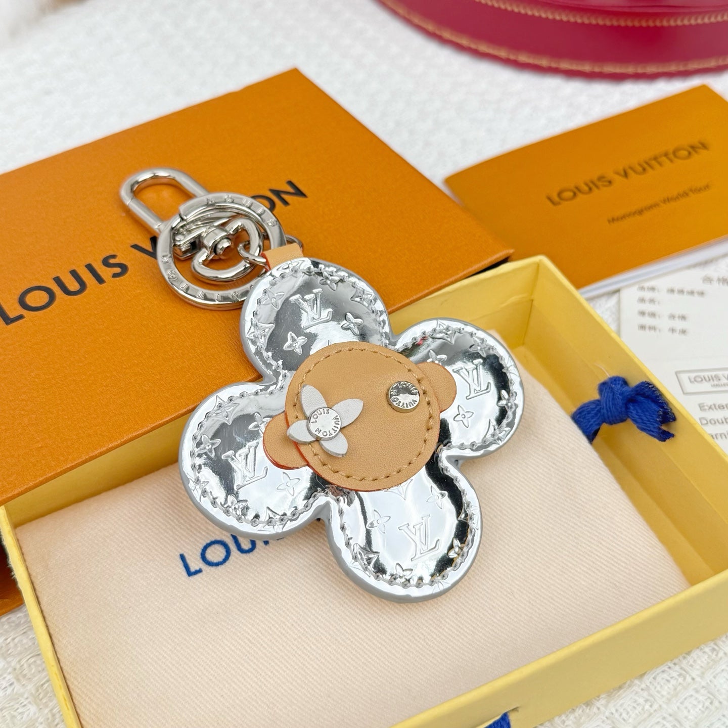 Flower-shaped keychain with silver monogram petals and tan leather center with metal clasp ring