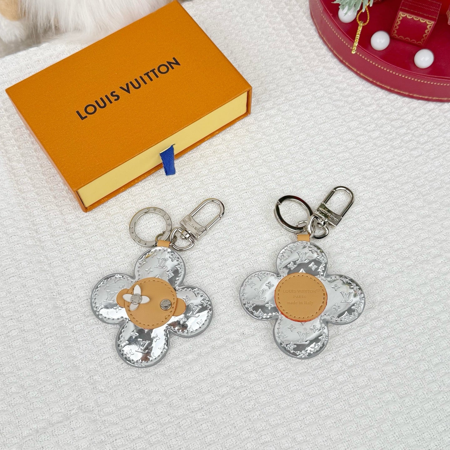 Louis Vuitton floral charm keyrings, silver monogram with tan centers, beside box