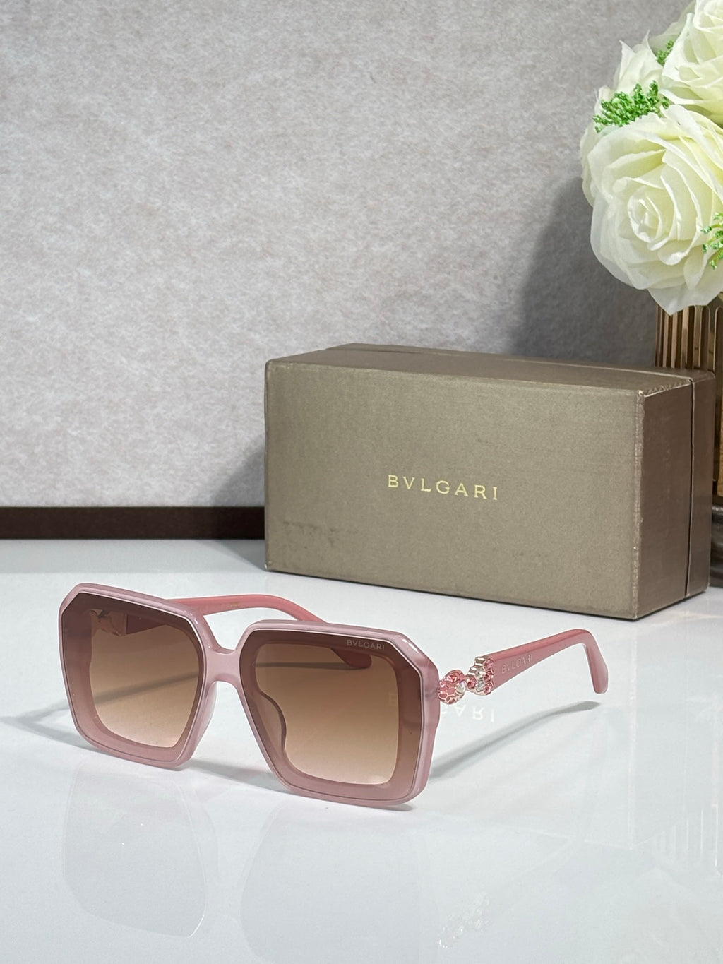 Bvlgari sunglasses with pink frames and tinted lenses, front view with jeweled temple accents.