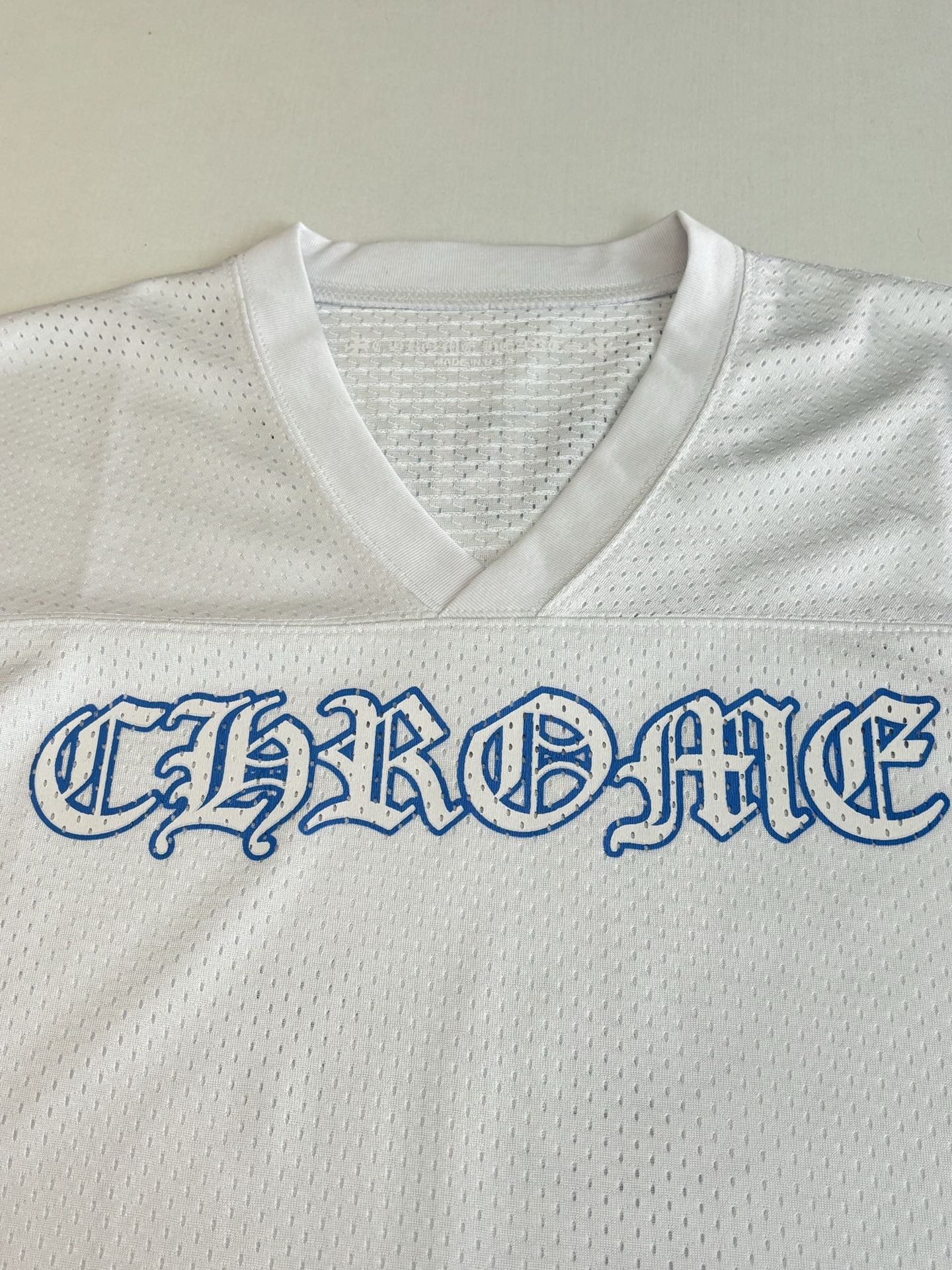 White V-neck jersey chest close-up with large blue embroidered-style word graphic