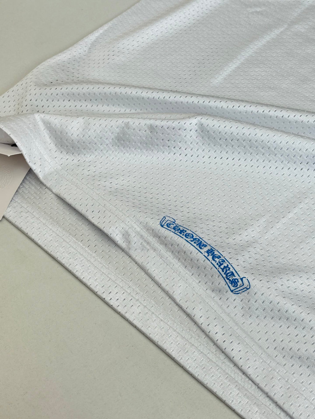White long-sleeve jersey fabric close-up with small blue logo near hem