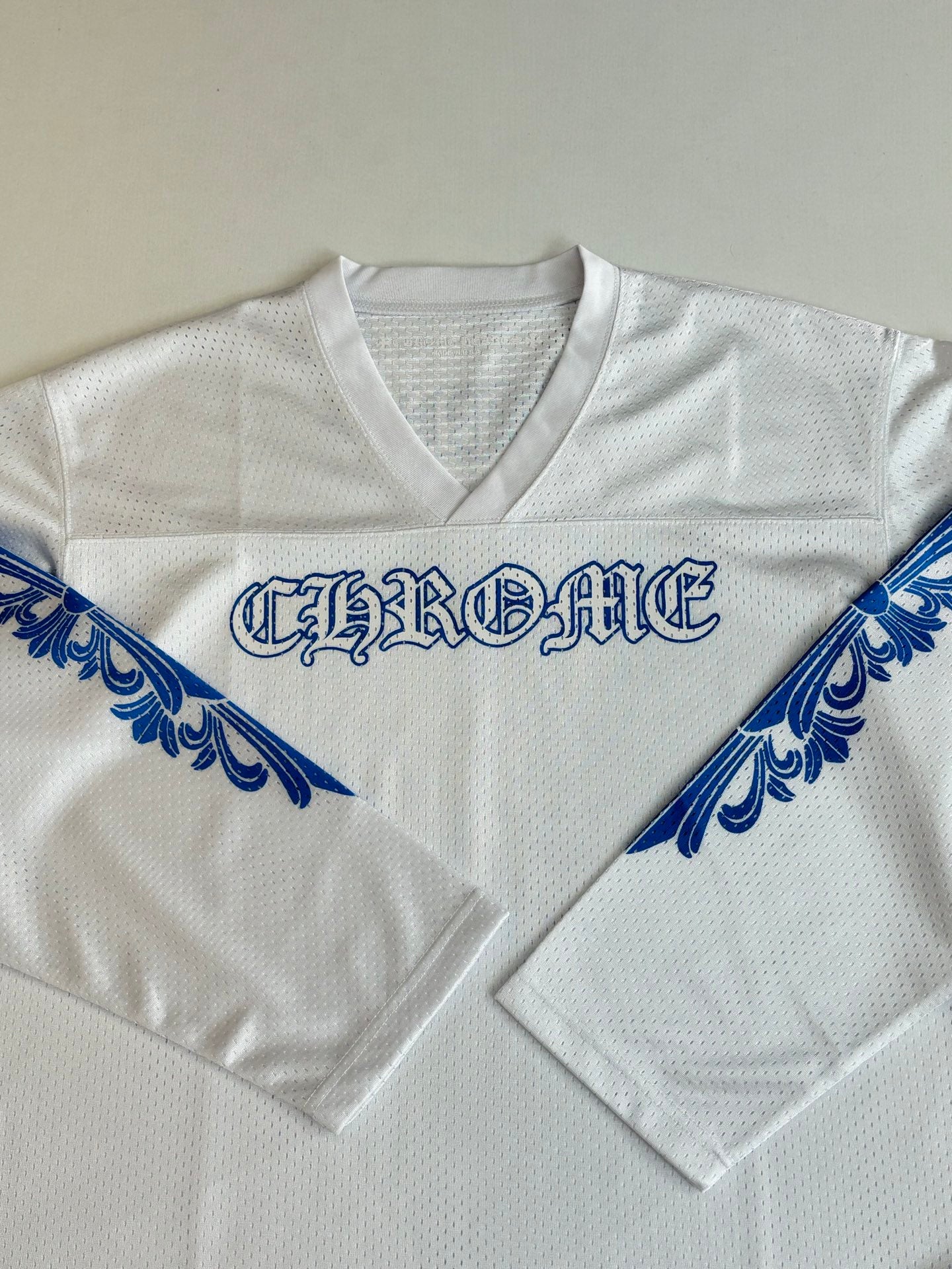 White V-neck jersey front close-up with blue logo across the chest and sleeves