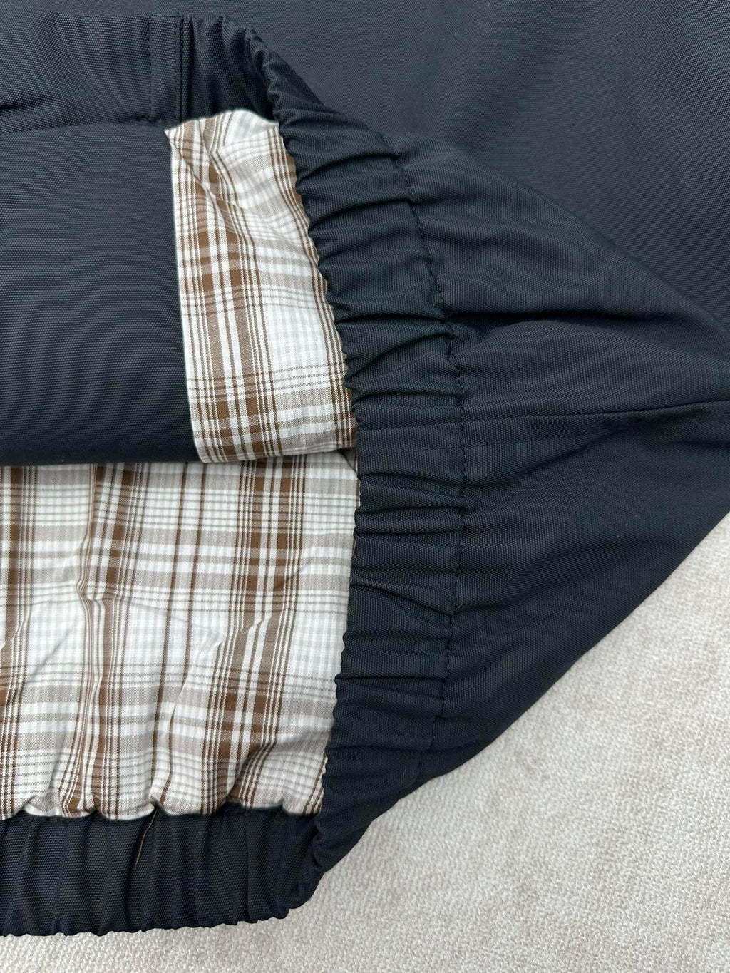 Dark jacket with plaid lining and elastic hem at inner opening