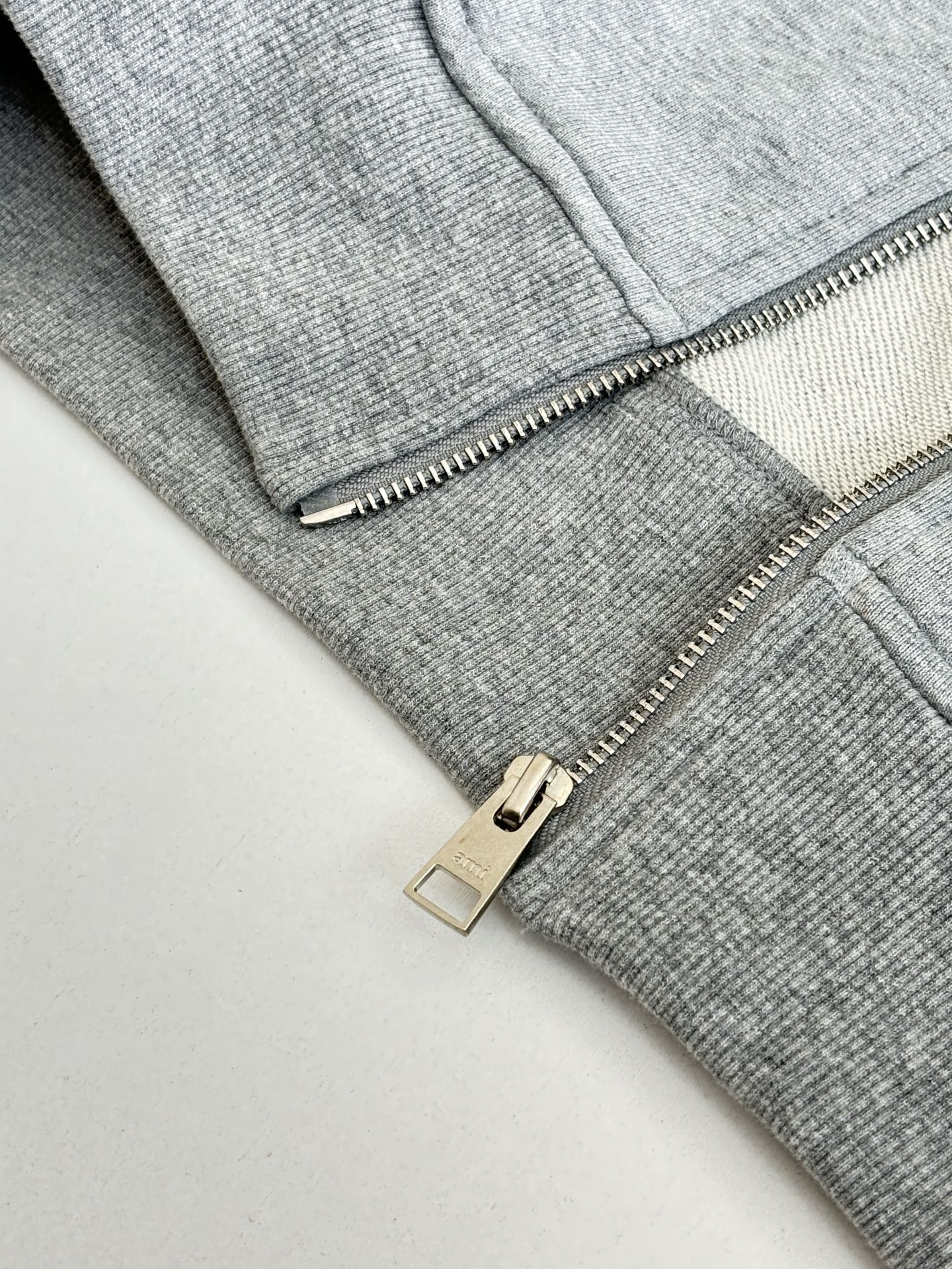 Amiri hoodie close-up of silver zipper pull and metal slider on light gray knit