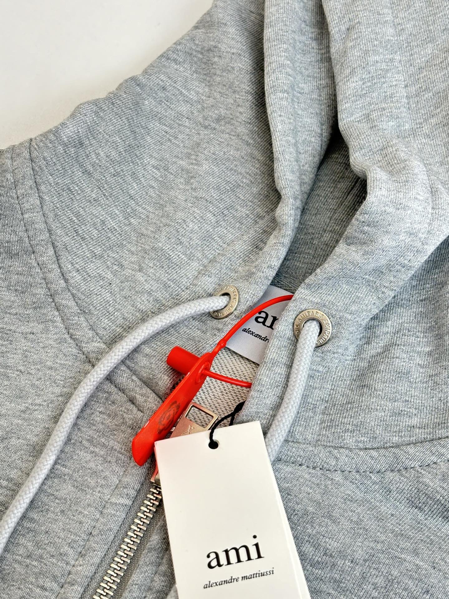 Amiri hoodie close-up of zipper, hood drawcord, and red tag with brand label