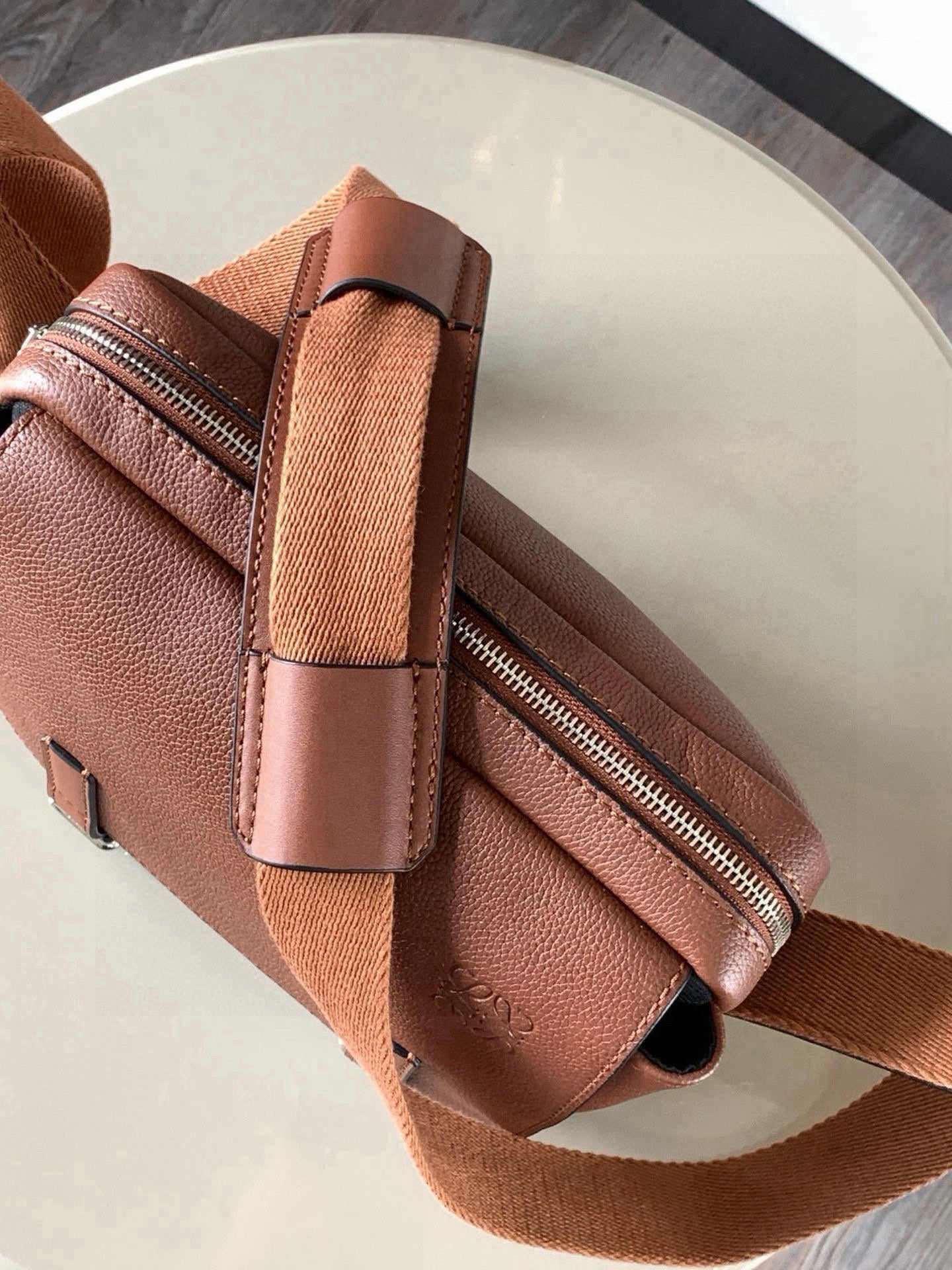 Leather crossbody bag detail showing front buckle, zipper, and strap tab