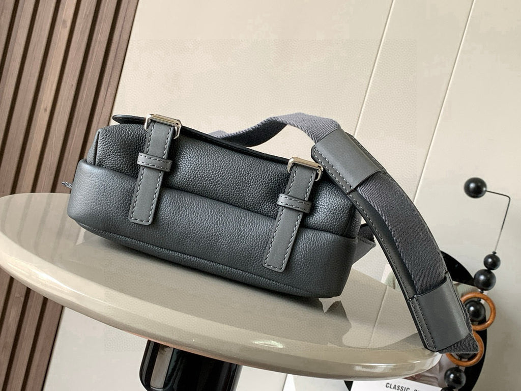 Gray leather crossbody bag with front buckle, flap top, and wide shoulder strap