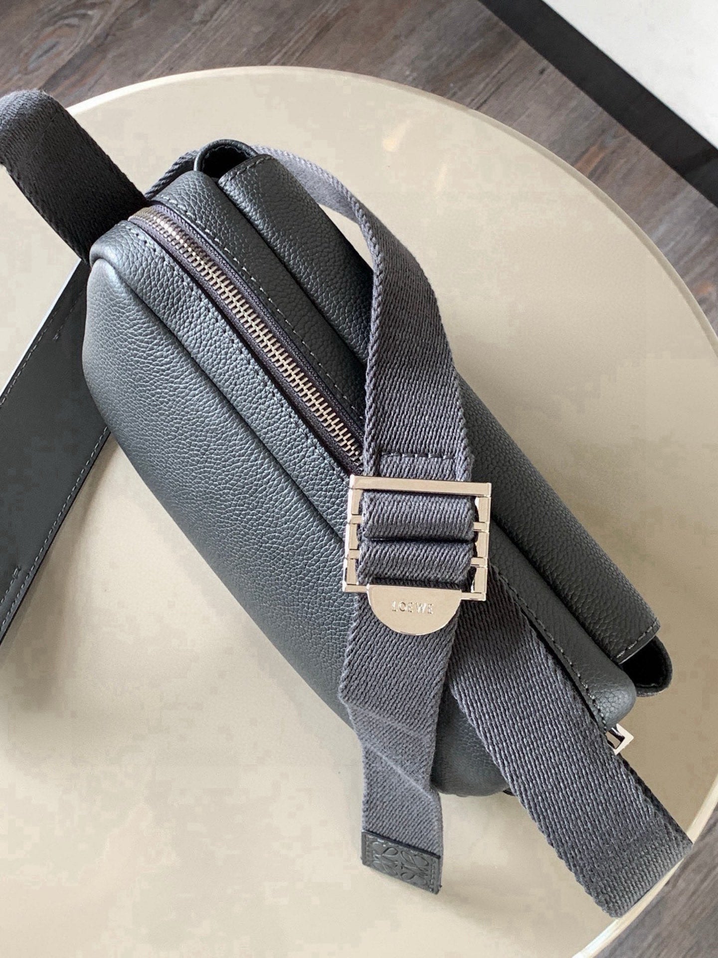 Gray leather crossbody bag with top zipper and adjustable strap with buckle
