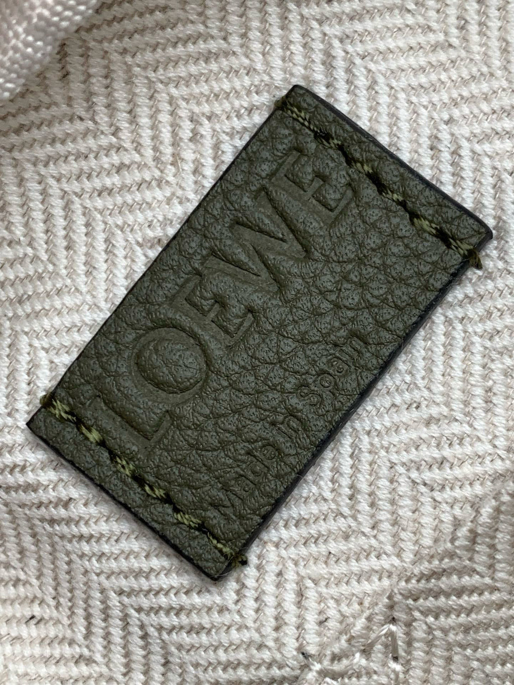 Embossed patch on sage green leather bag, showing partial Loewe lettering