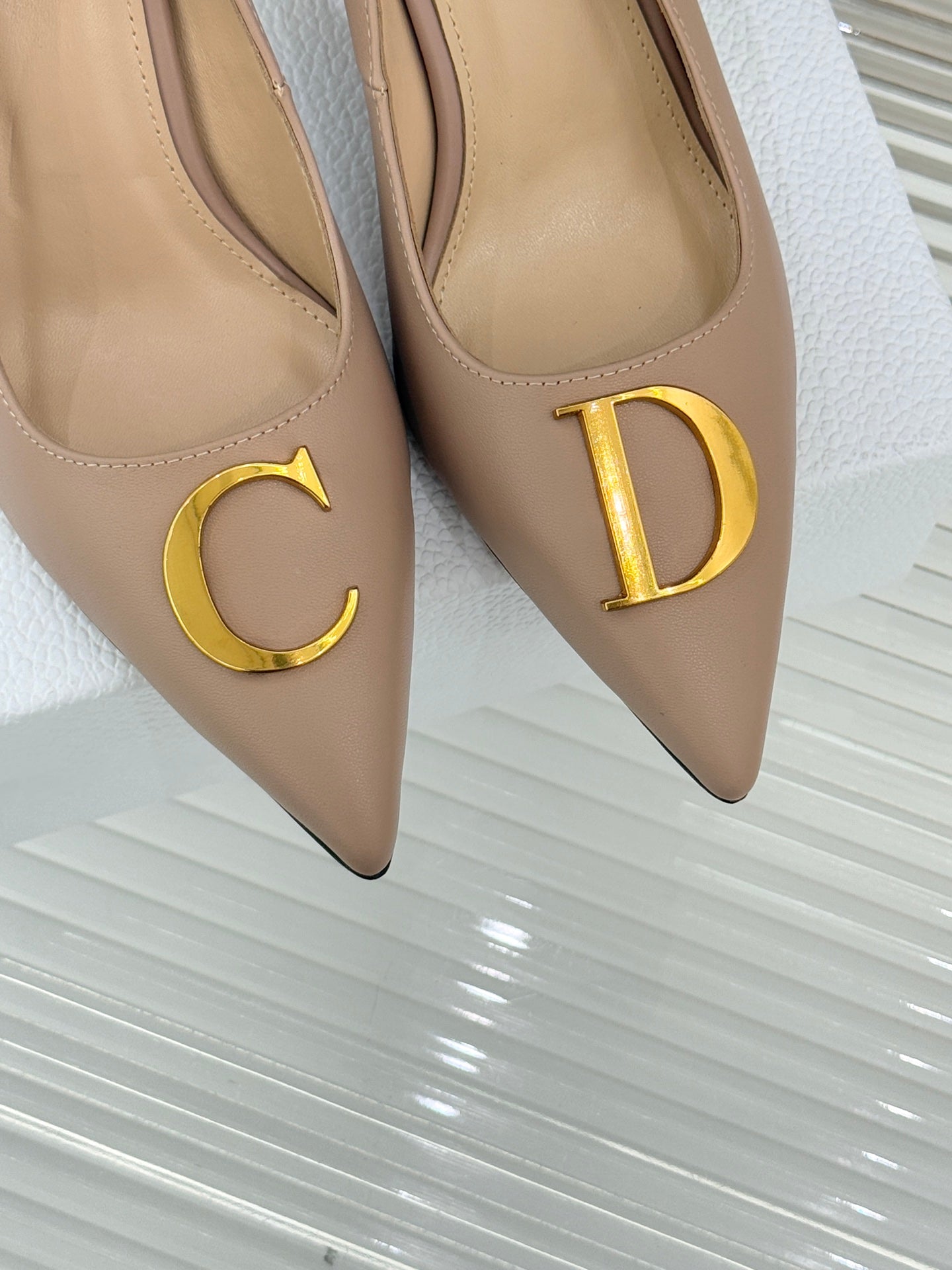 Beige Dior pointed-toe stiletto pumps close-up showing gold C and D logo