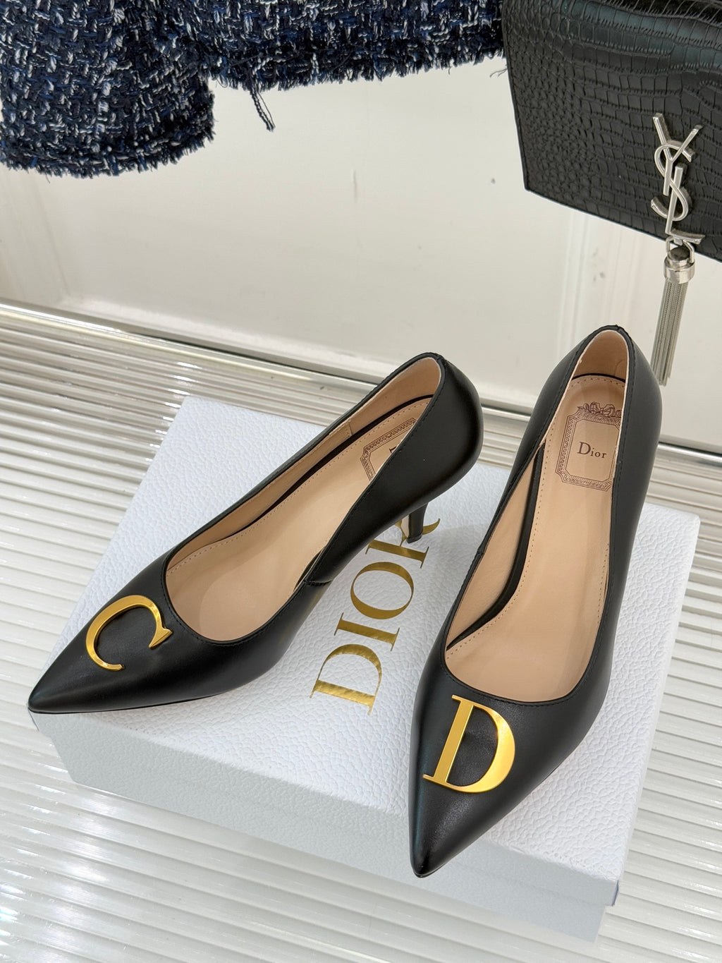 Black pointed-toe pumps on a white box with gold D logo detail