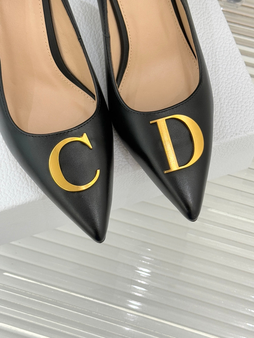 Close-up of black pointed-toe pumps with gold C and D front emblems