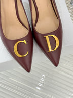 Maroon pointed-toe pumps with gold C and D monogram on front