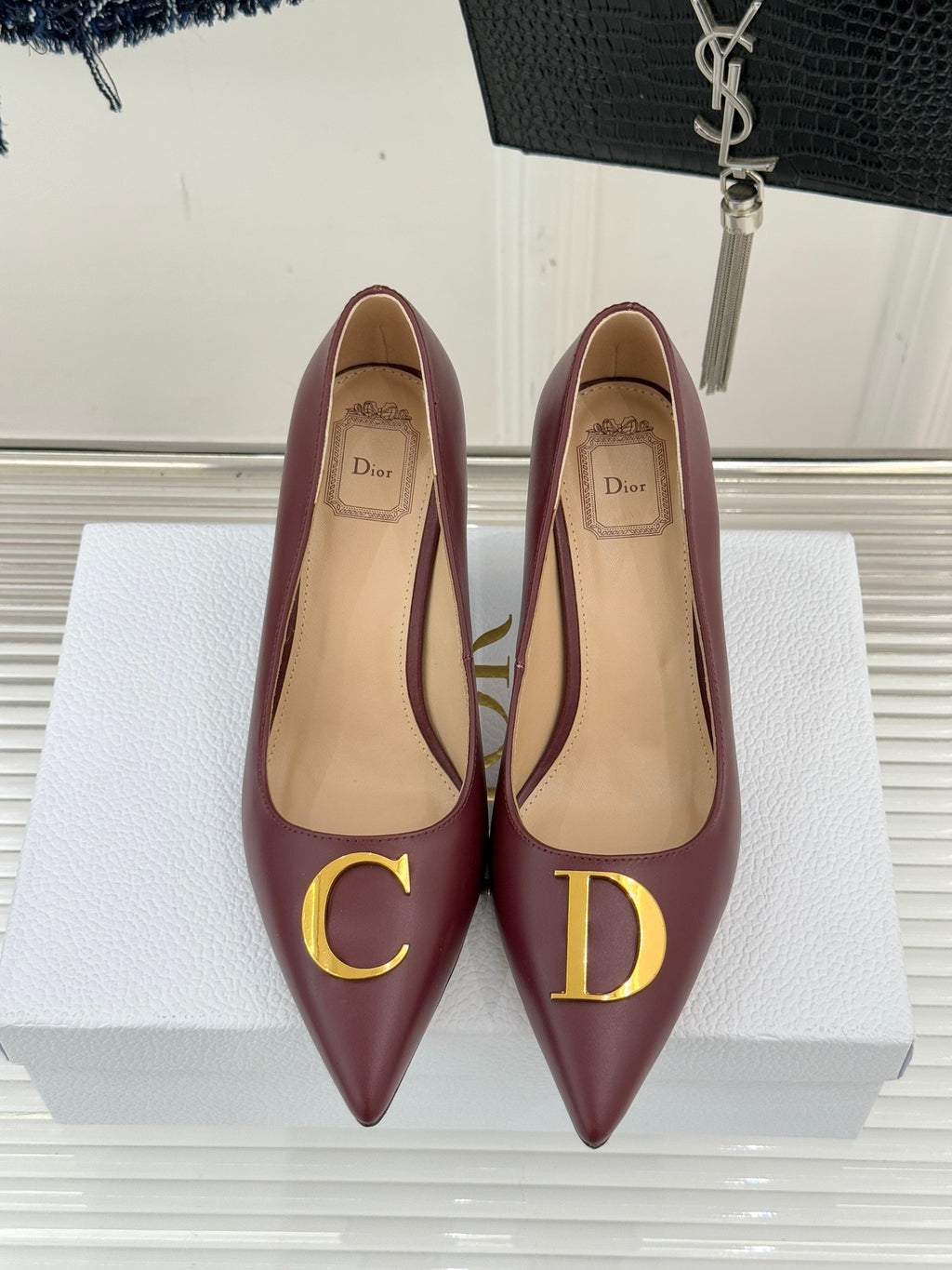 Maroon pointed-toe stiletto pumps with gold D emblem, heel view