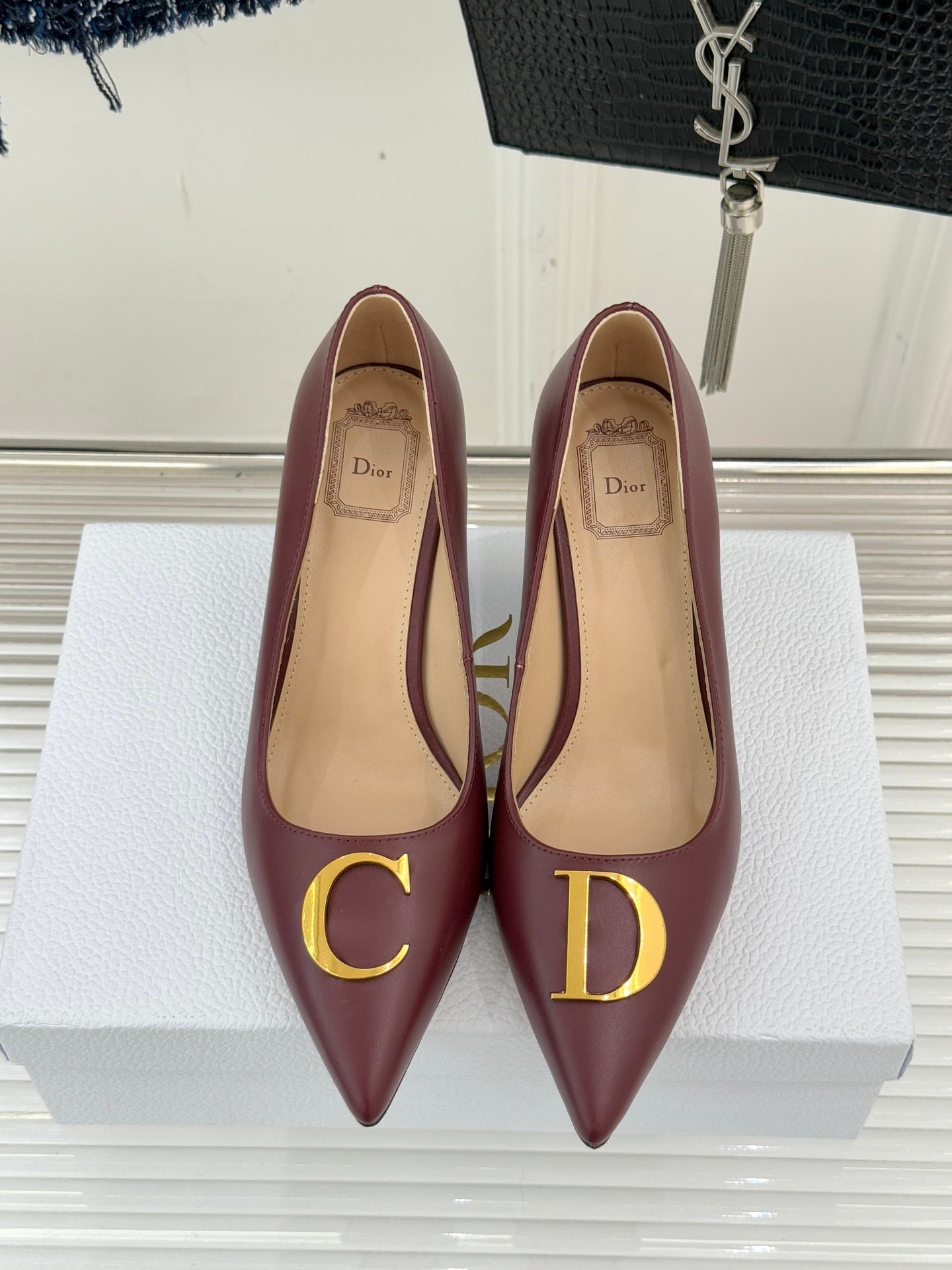 Maroon pointed-toe stiletto pumps with gold D emblem, heel view