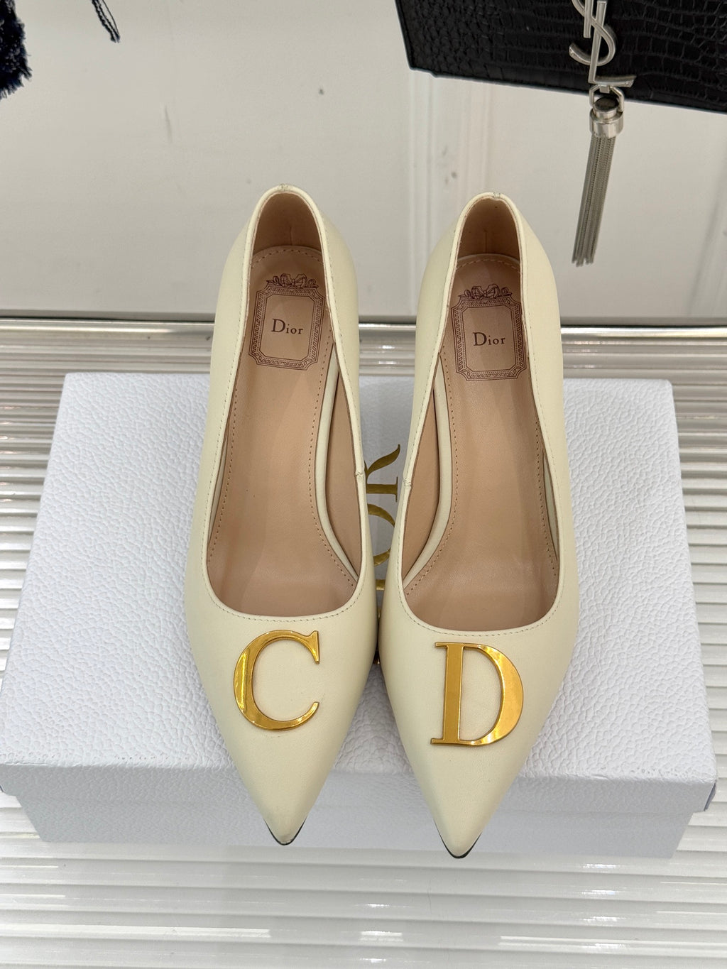 Pair of cream pointed-toe high-heel pumps with gold D logo on toe