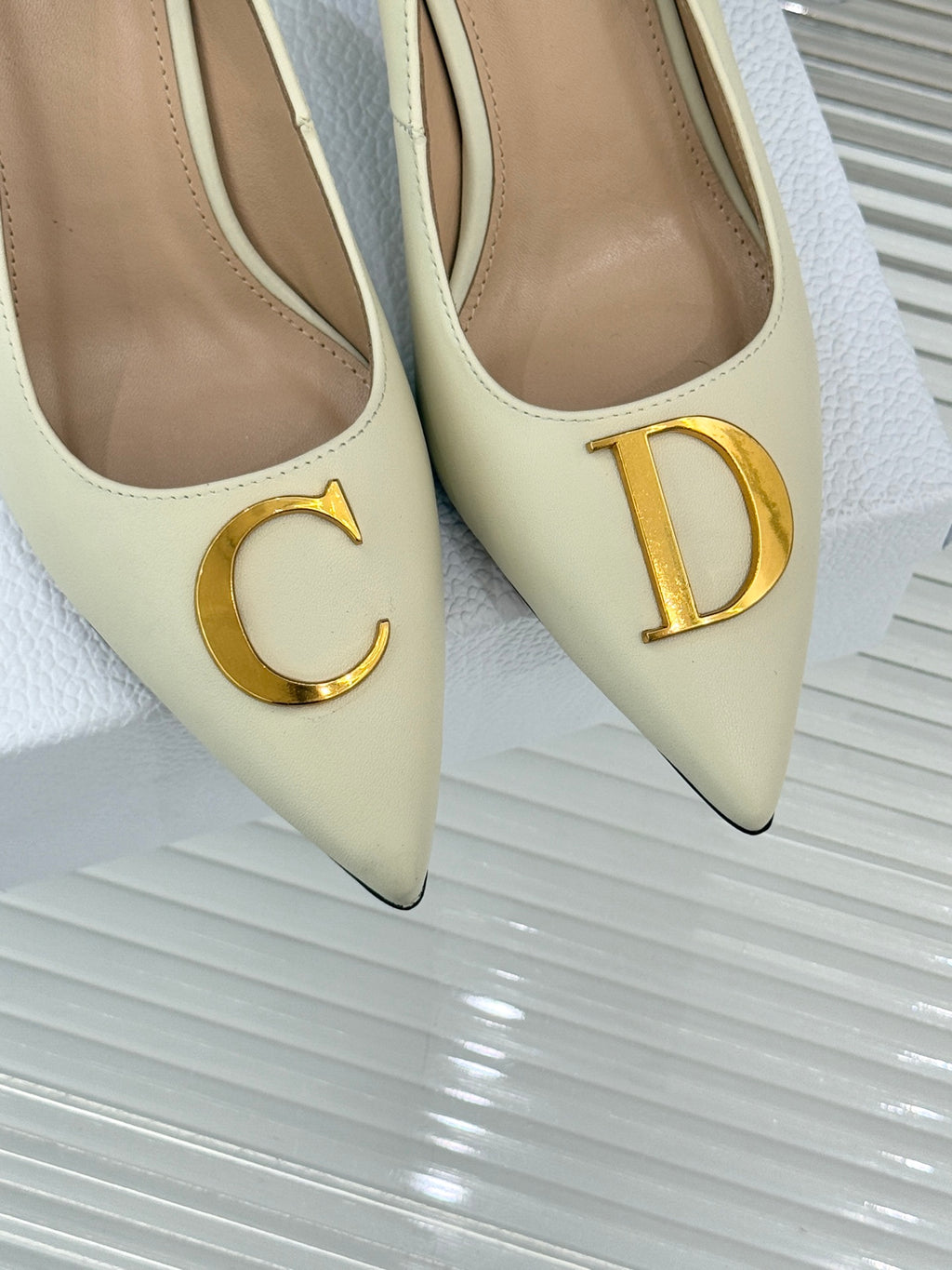 Cream pointed-toe high-heel pumps with gold C and D logo emblems