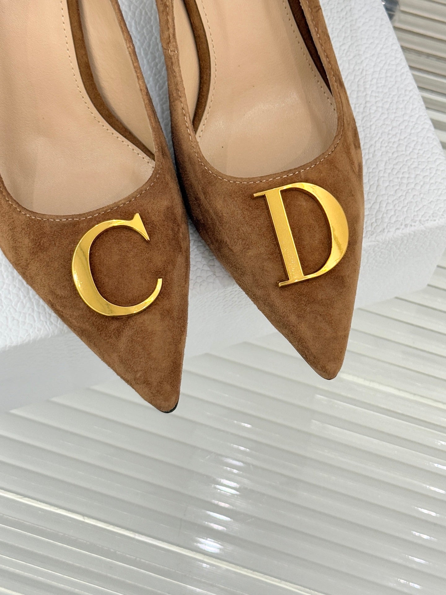 Tan suede pointed-toe pumps with gold C and D logo emblems