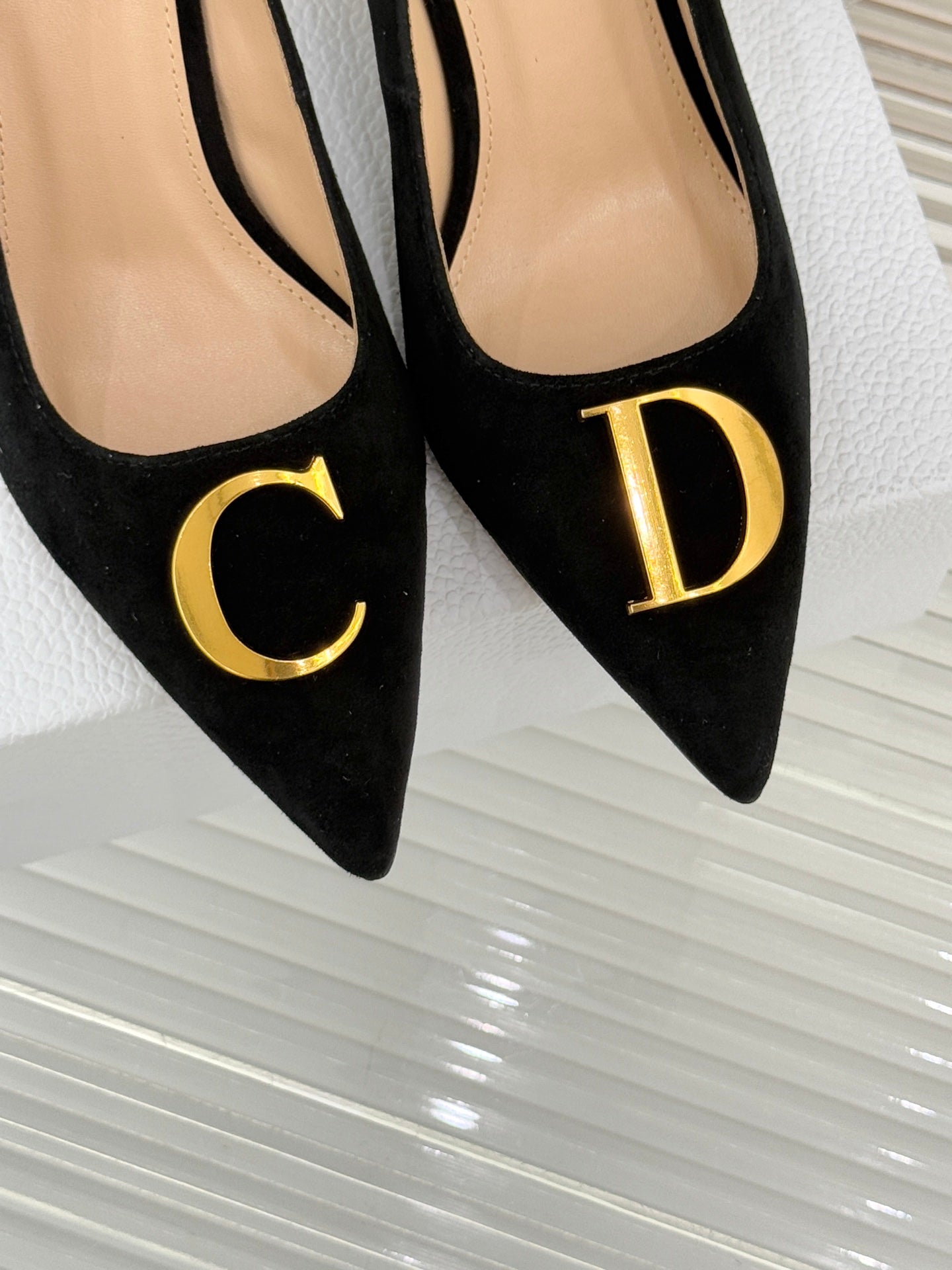 Black suede pointed pumps close-up with gold C and D logo accents