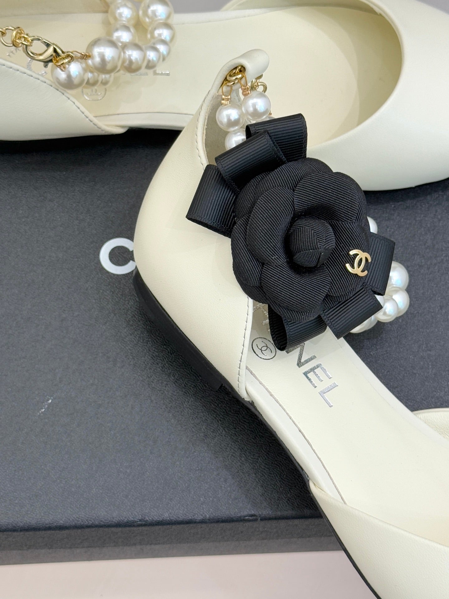 Chanel ladies' cream flats with black bow ornament and pearl detail on strap