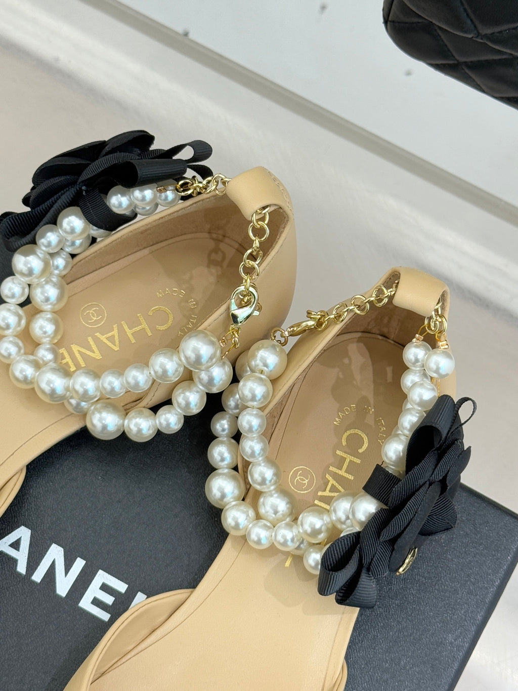Chanel beige flats with black bows and faux pearl straps, shown from side angle