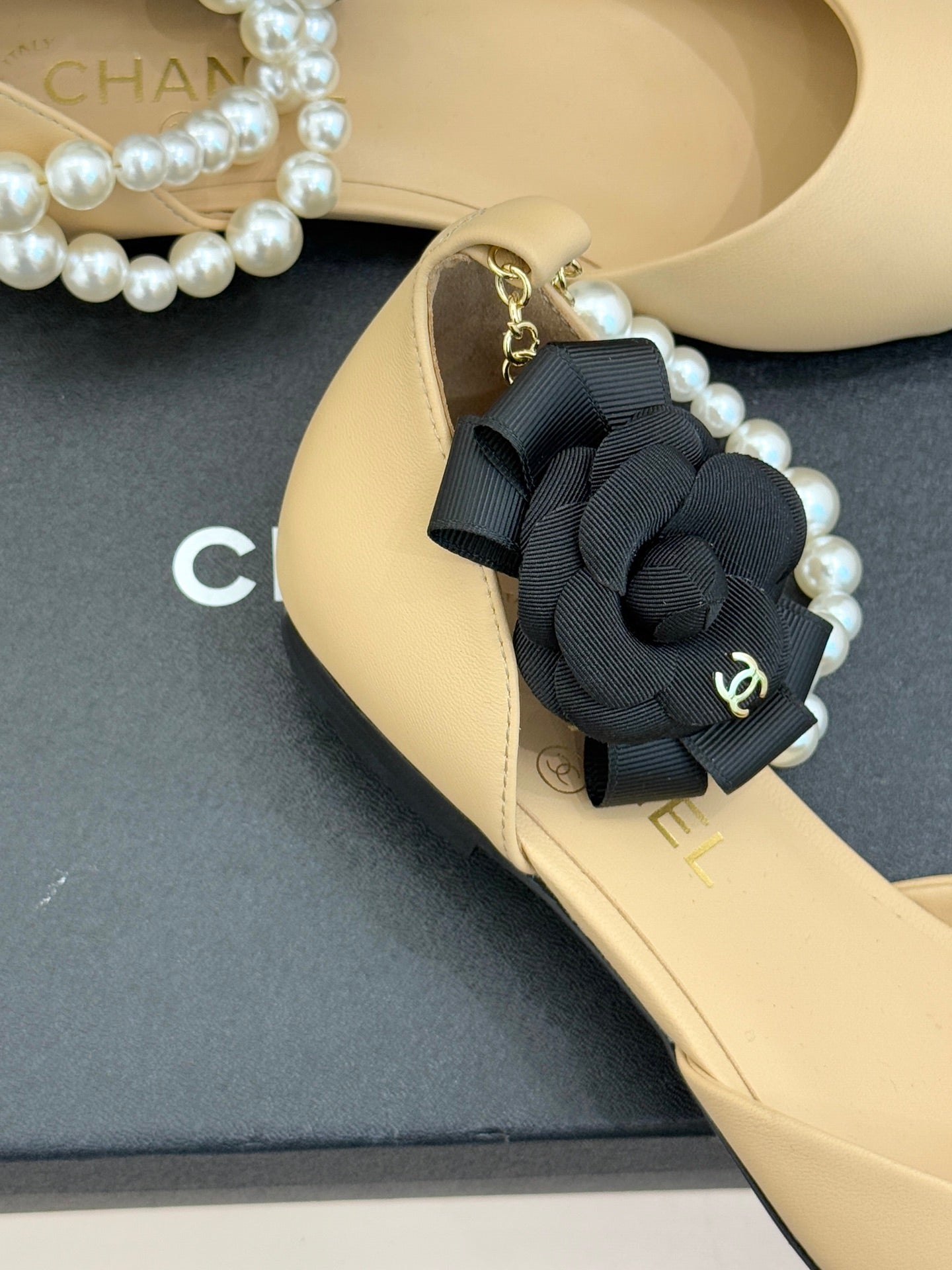Close-up of Chanel beige flat with black bow, faux pearls, and gold chain detail