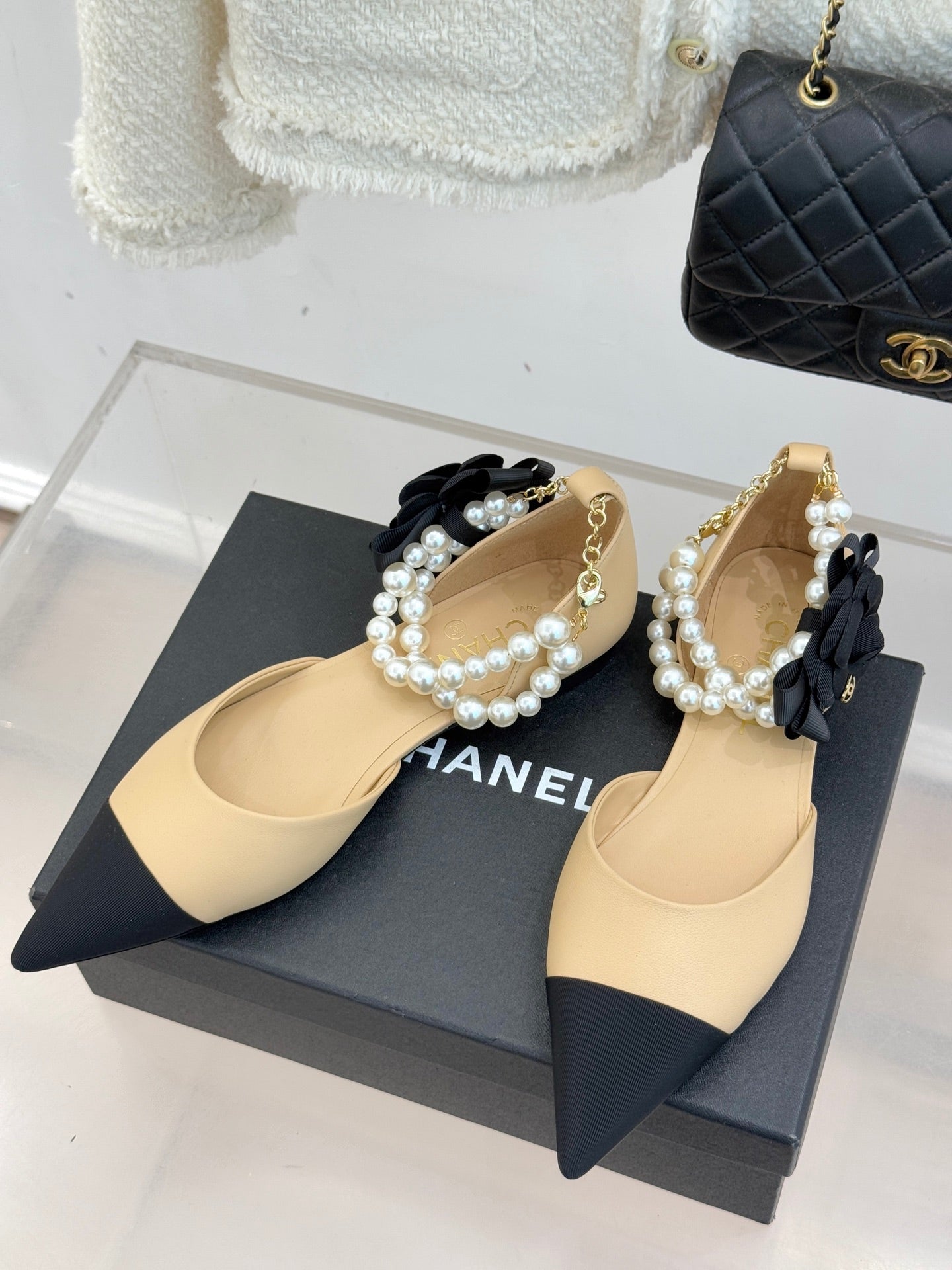 Pair of Chanel flats with beige pointed toes, black bow accents, and faux pearl trim