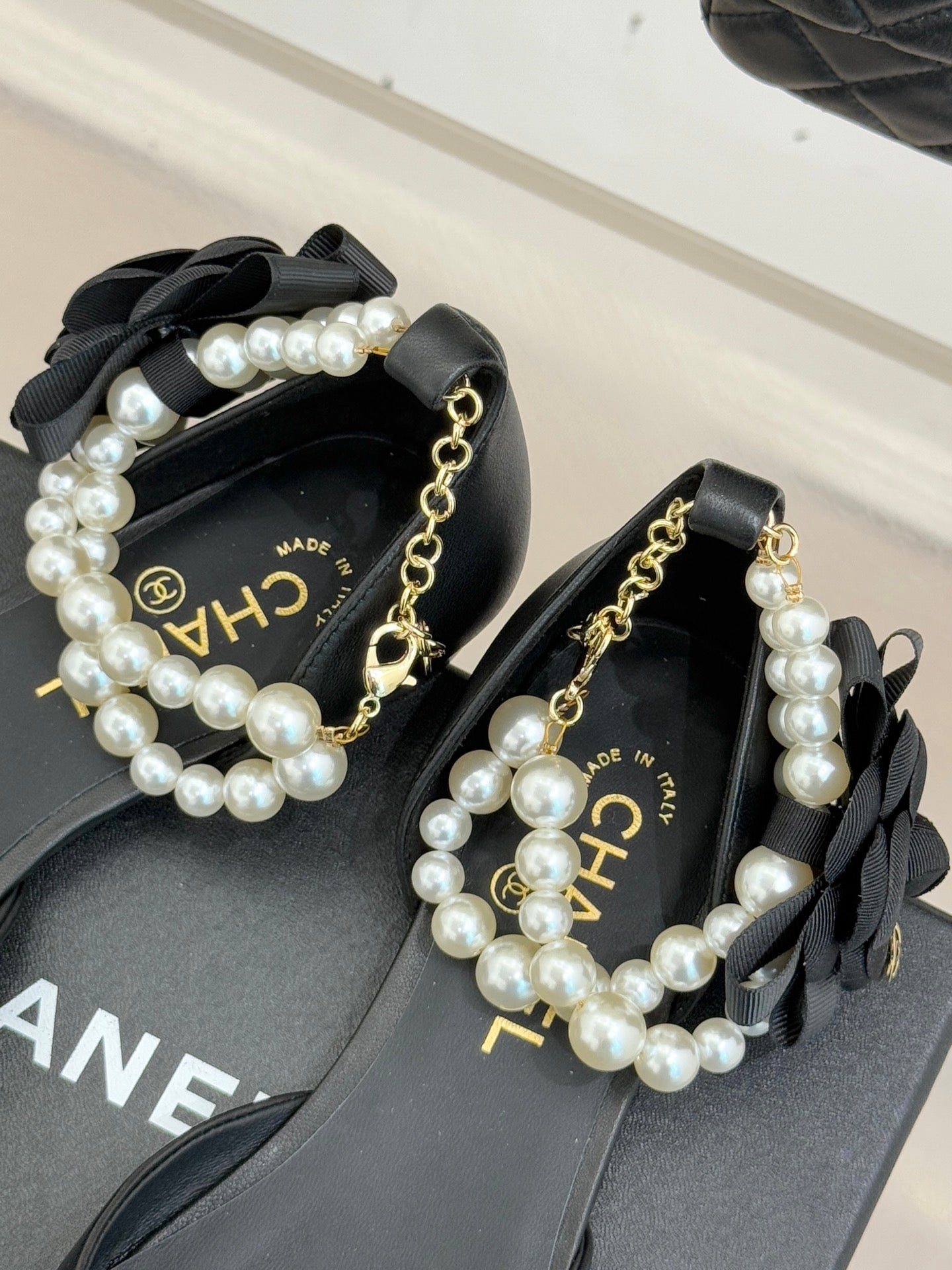 Chanel ladies black mules with faux pearl straps, gold chain, and CHANEL detail
