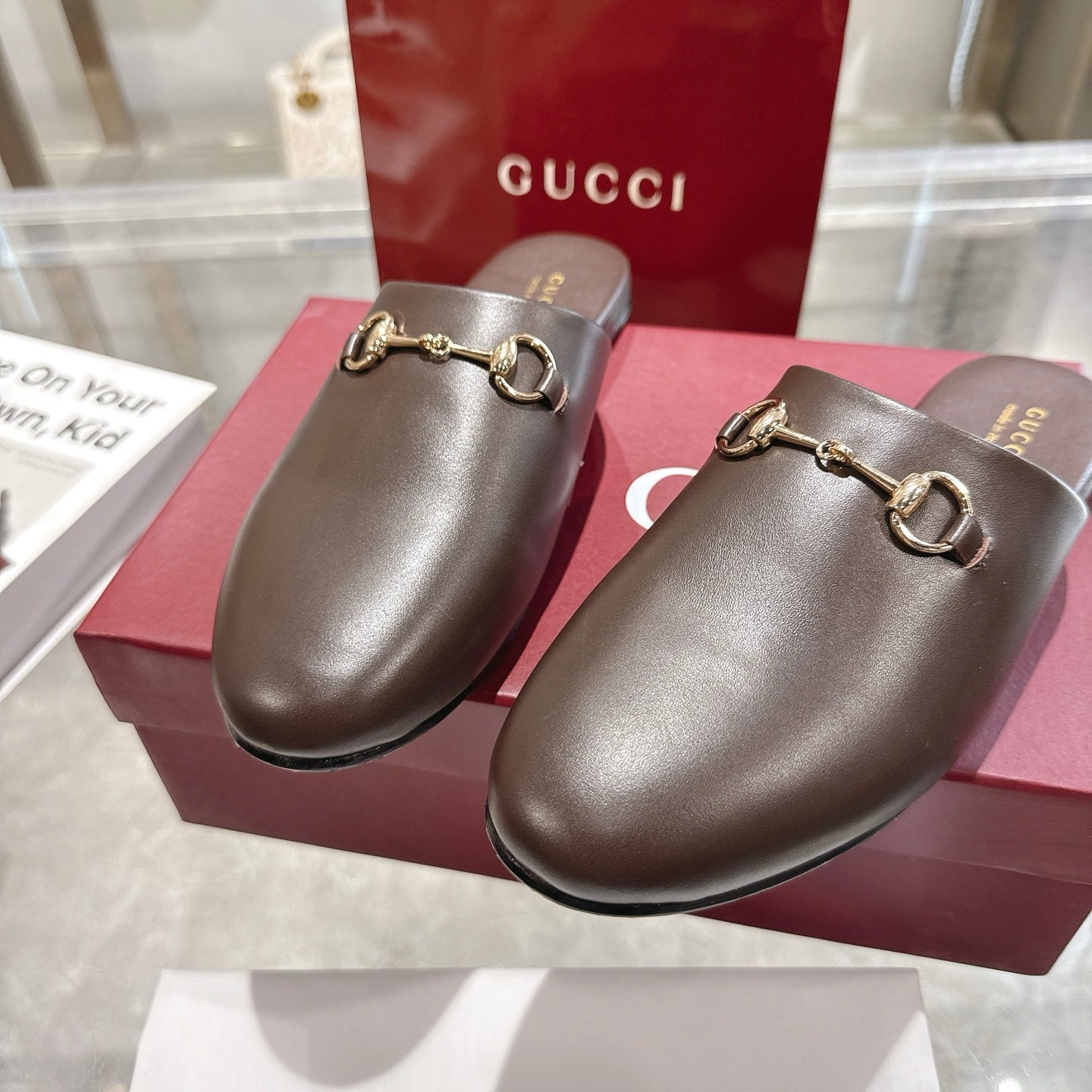 Gucci unisex dark leather mules with gold-toned horsebit buckle detail and rounded toe.