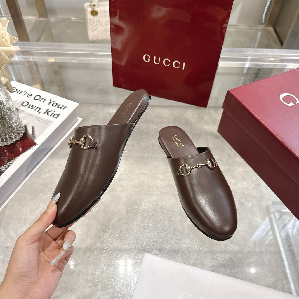 Gucci unisex leather horsebit mules with rounded toe, shown with a hand for scale.