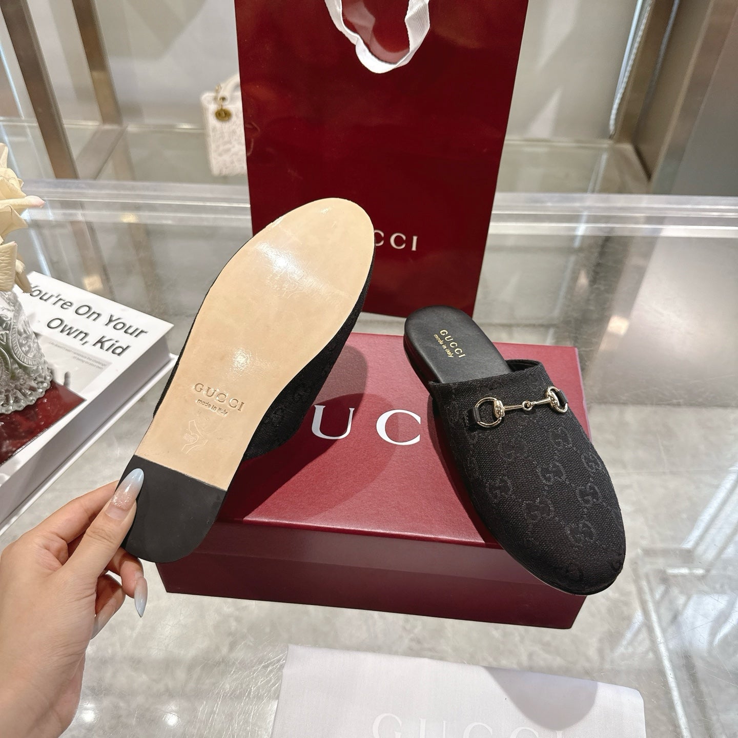 Gucci unisex mules with dark monogram upper; hand holds light sole underside view