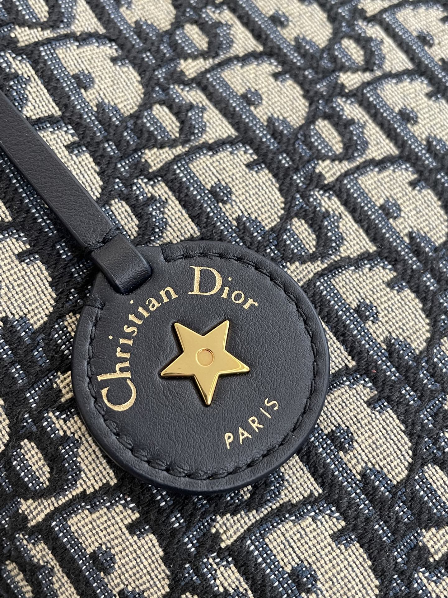 Round emblem patch on navy-and-beige Dior monogram bag with gold star