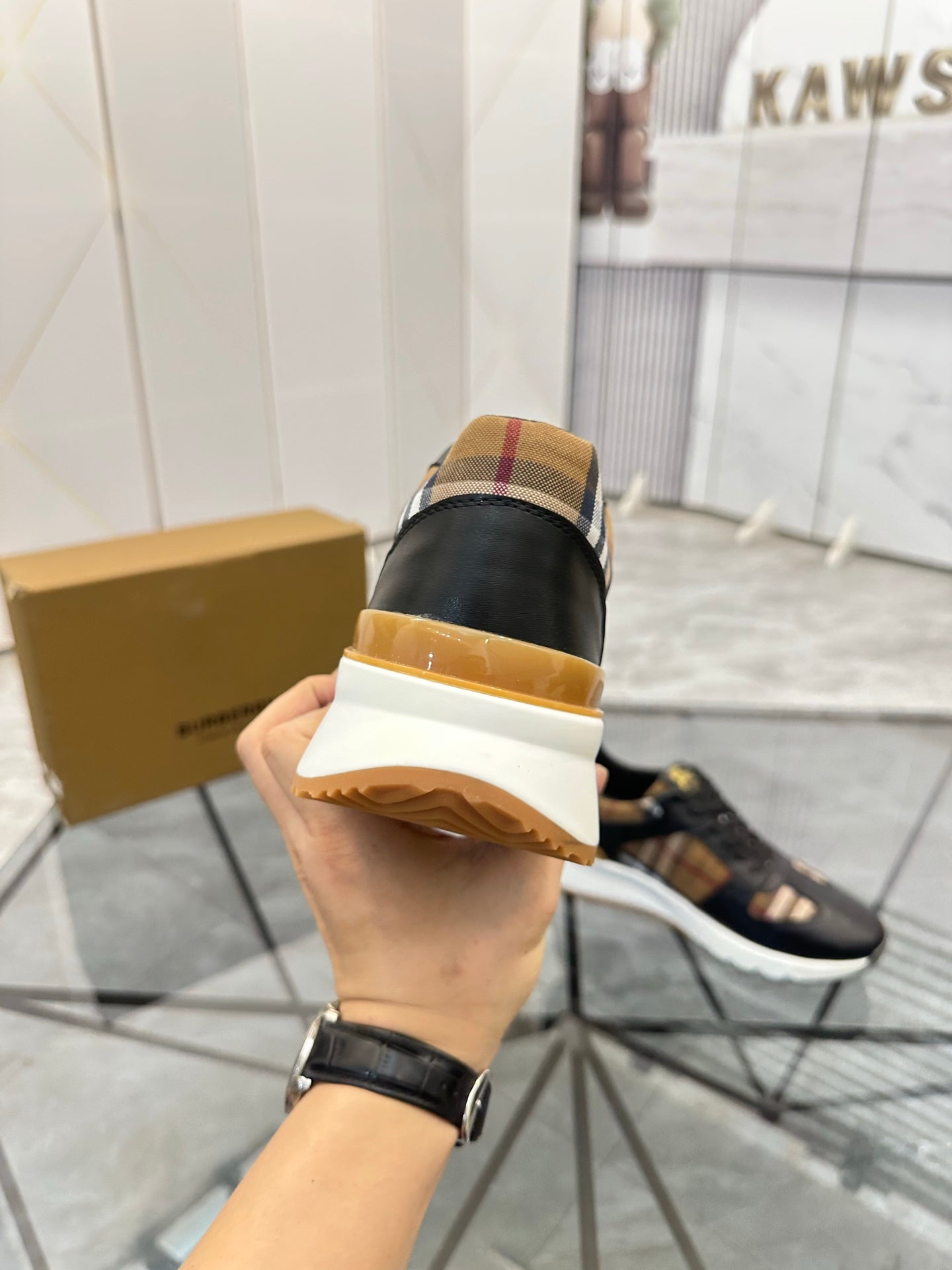 Black sneaker heel view in hand with tan-gold trim and cushioned sole