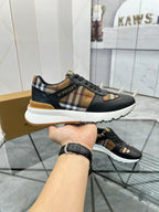 Black lace-up sneaker held in hand, plaid side panel and gold-brown trim