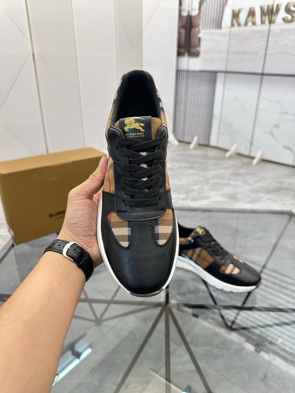 Black lace-up sneaker held up, textured sole and gold logo patch