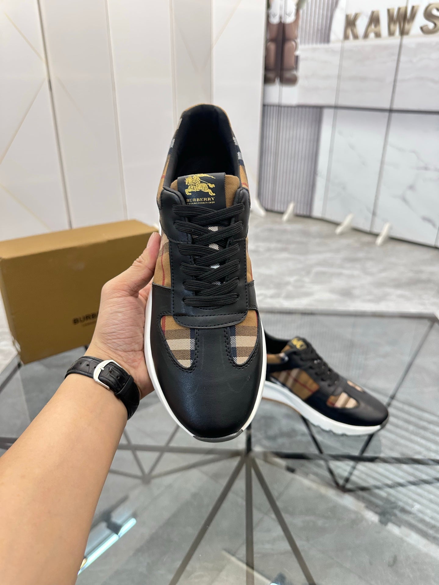 Black lace-up sneaker held up, textured sole and gold logo patch