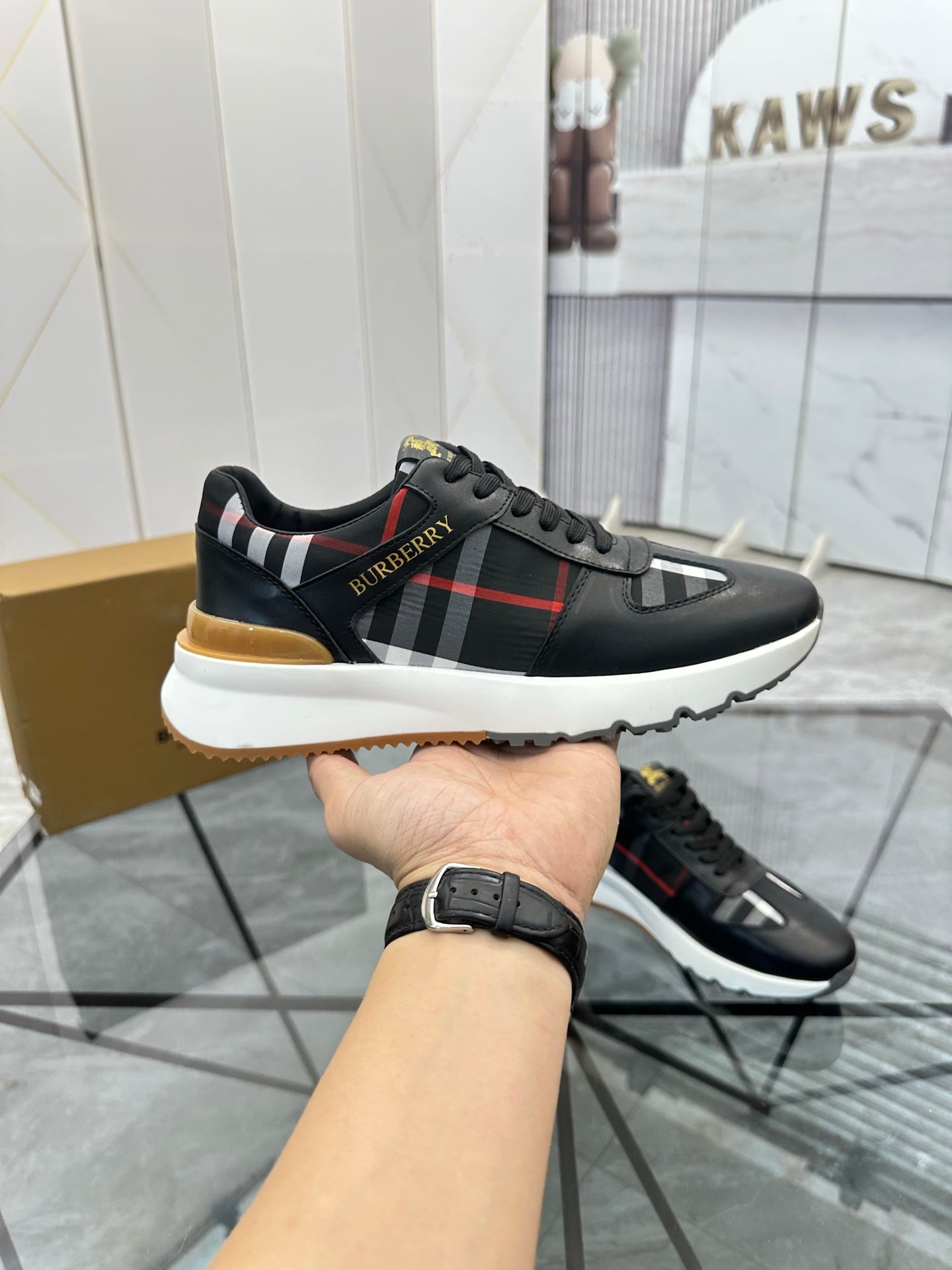Black low-top sneaker with plaid side stripe, red line, and gum sole edge