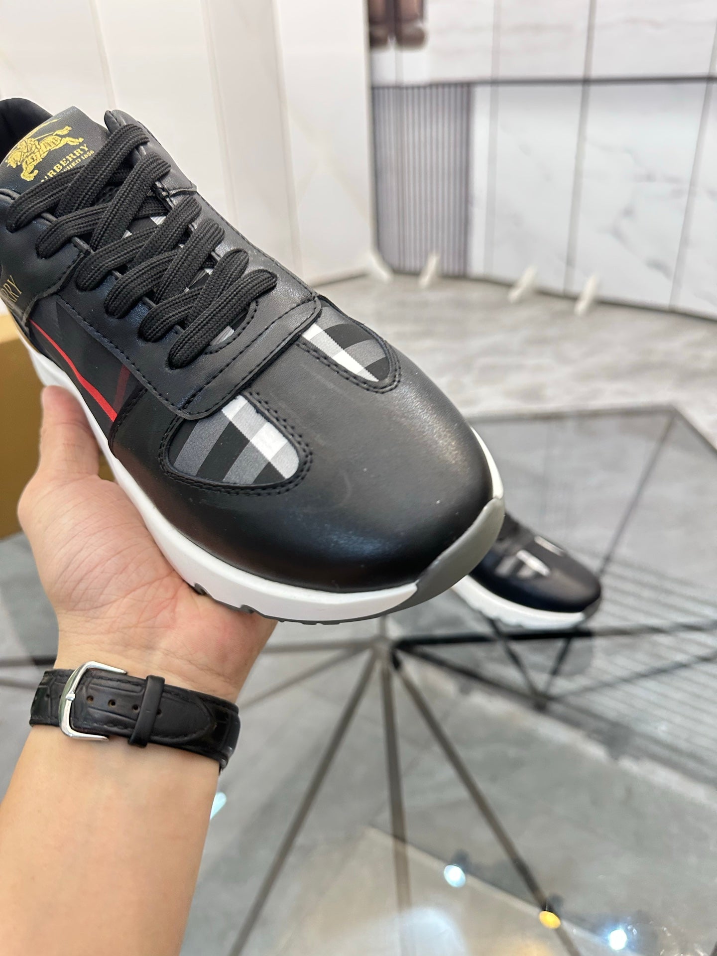 Black low-top sneaker close-up with black laces, plaid panel, and white midsole