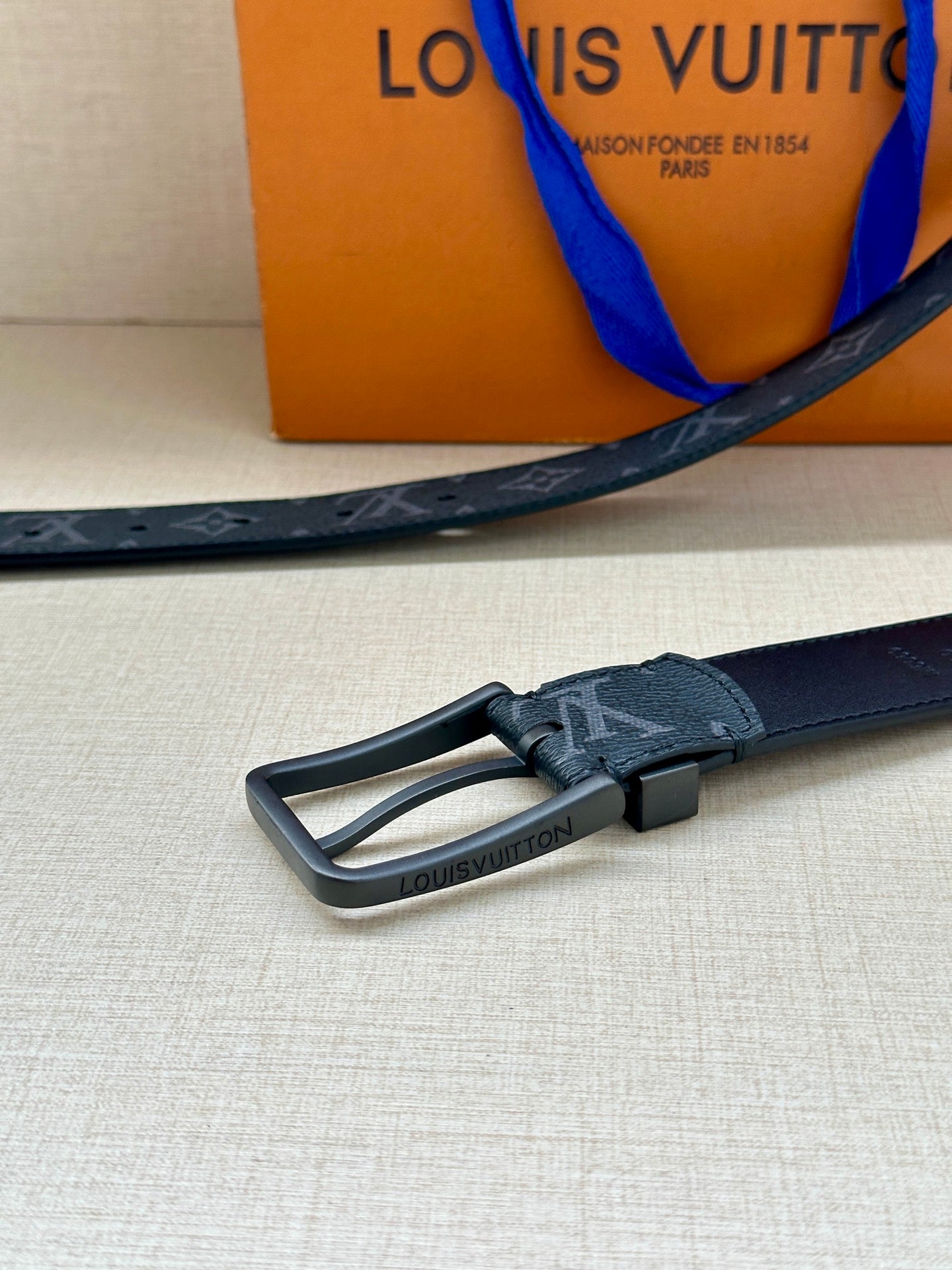 Louis Vuitton belt buckle close-up on dark blue monogram strap with silver-tone frame