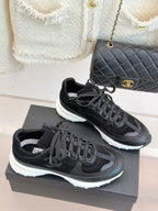 Chanel women’s lace-up sneakers in dark black, 3/4 view on a gray presentation box.