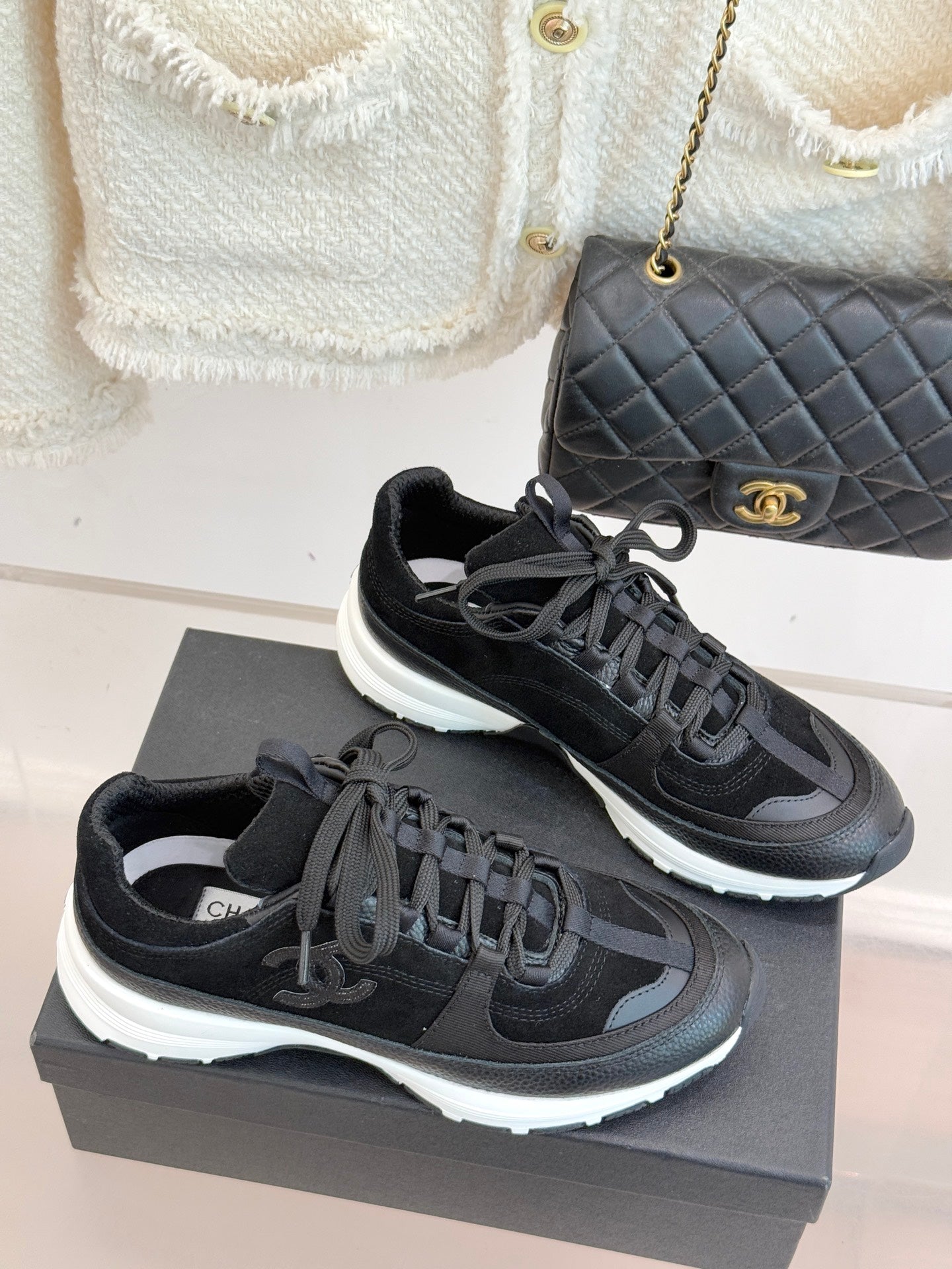 Chanel women’s lace-up sneakers in dark black, 3/4 view on a gray presentation box.
