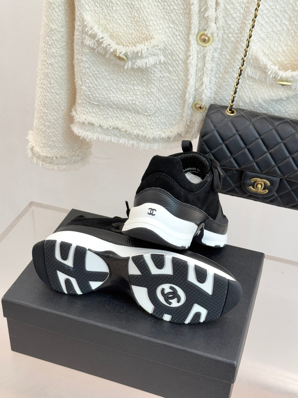 Chanel women’s sneakers, black pair with patterned outsoles visible on a gray box.