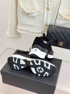 Chanel women’s sneakers, black pair with patterned outsoles visible on a gray box.